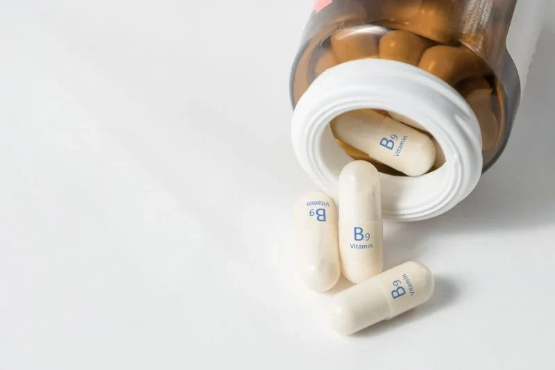 A bottle of Vitamin B9 supplements spilling onto a white surface, highlighting the advantages of Vitamin B Complex for overall health.